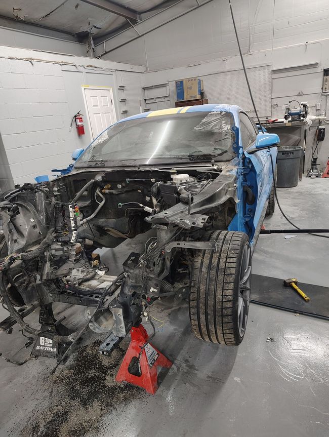 Person in green gloves spray painting a car white in a workshop.