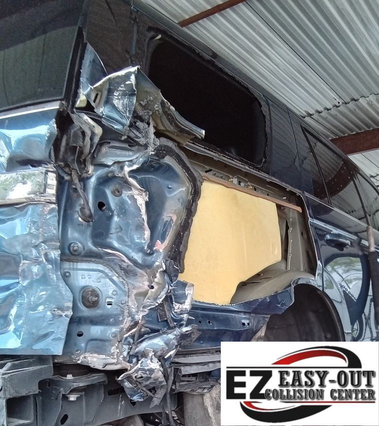 Damaged blue car rear with severe impact damage, at Easy-Out Collision Center.