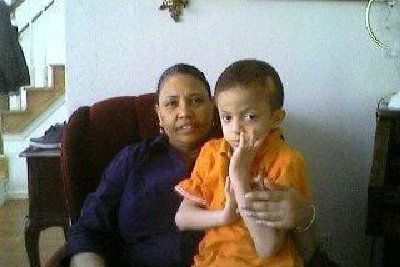 Woman in blue shirt with a child in orange shirt. They sit in a chair indoors.