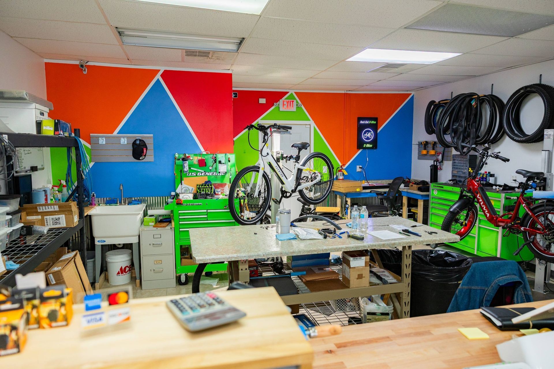 Bright workshop with colorful wall art, tools, bikes, and workbenches in a cluttered repair space