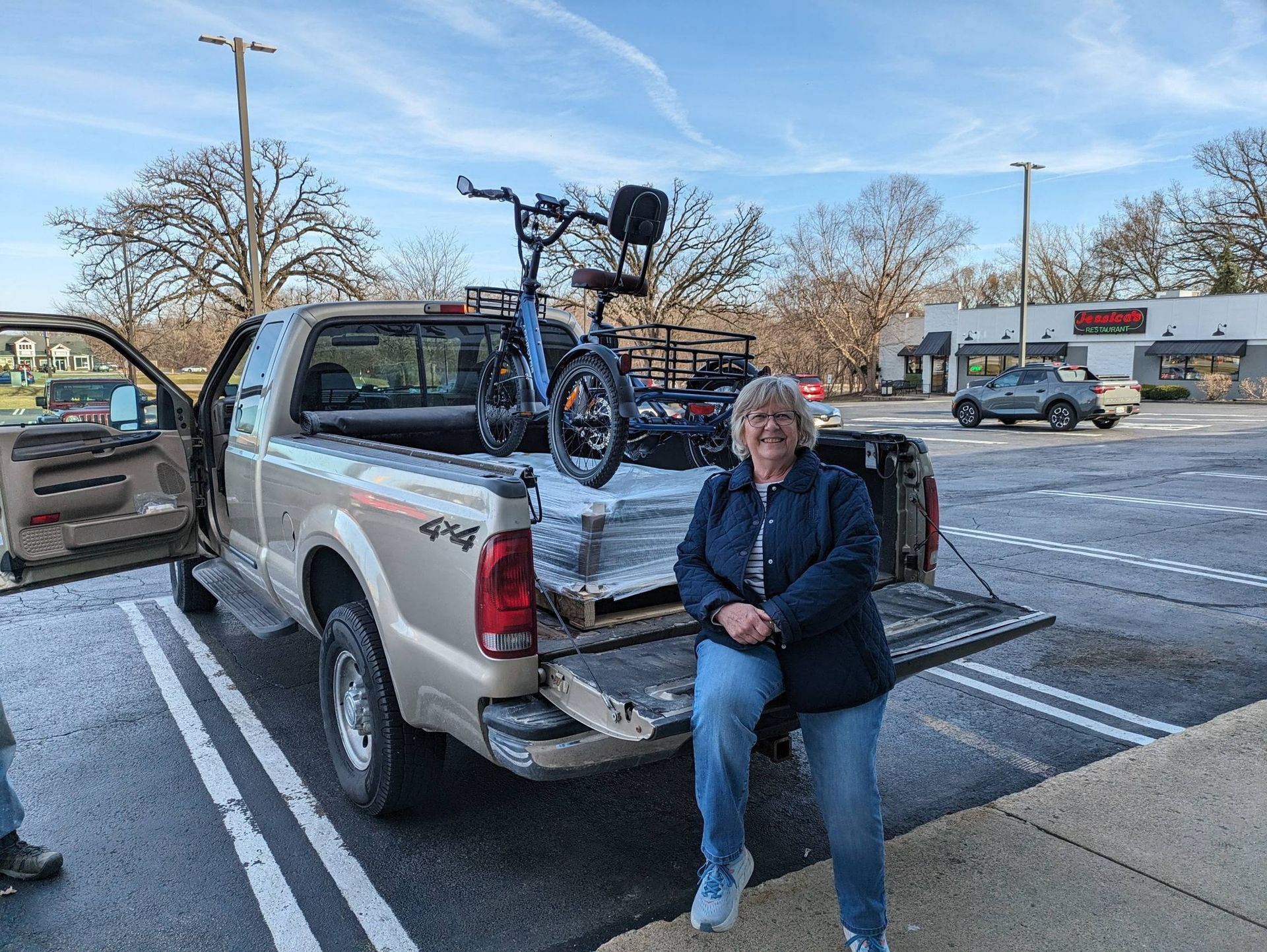 Woman sitting on a pickup truck tailgate beside a bicycle in a snowy parking lot