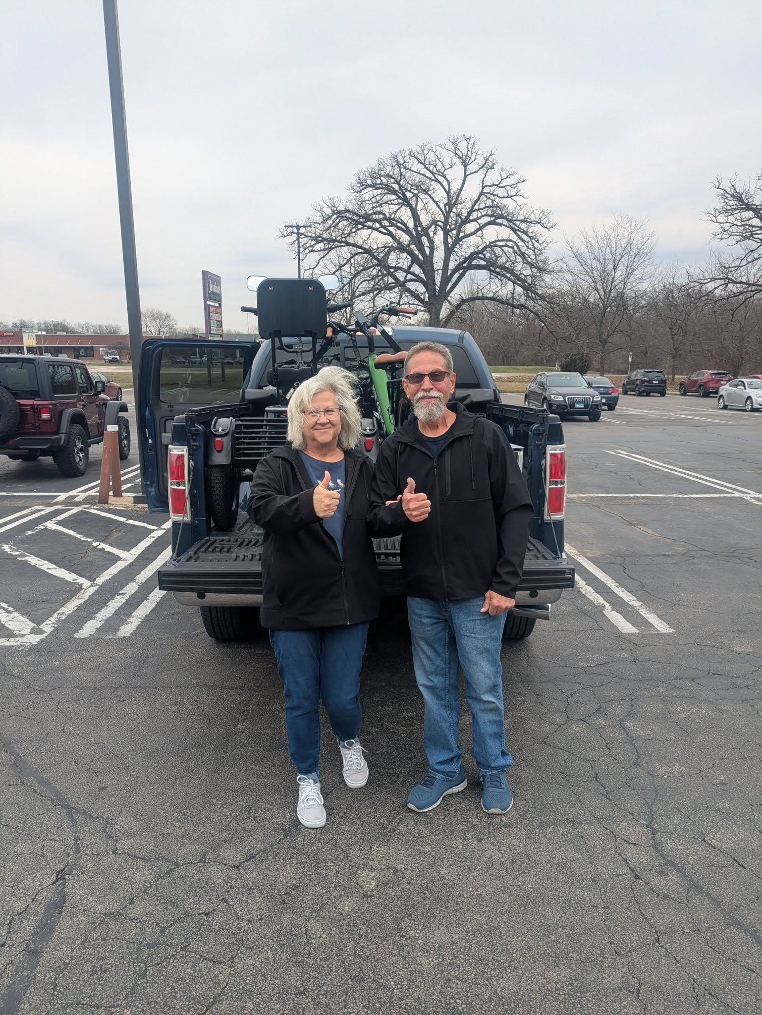 Two people standing in a parking lot, smiling and holding drinks near a truck with cargo equipment.