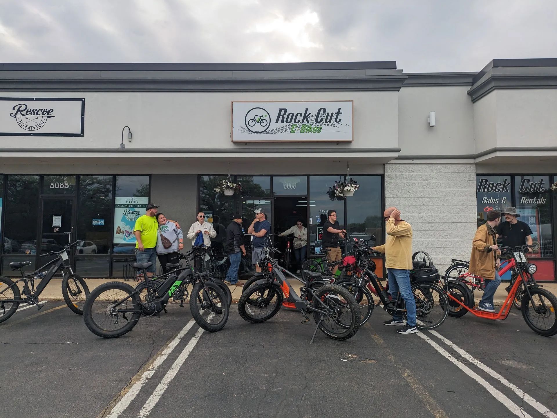 Group of cyclists posing with bikes outside a Black Fox Coffee shop at a strip mall.
