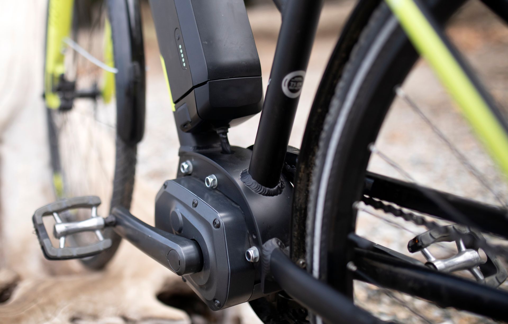Close-up of an electric bicycle's mid-drive motor and pedal near a rear wheel.