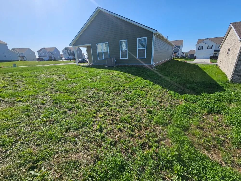 A house with dark siding sits on a grassy hill. Clear sky.