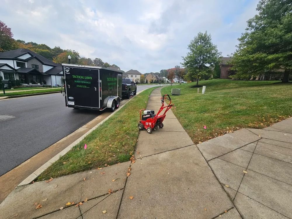 A red lawn edger on a sidewalk, near a trailer and houses in a residential neighborhood.