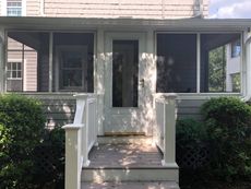 Front porch with a white door, screen windows, and shrubbery.