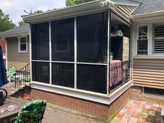 Screened-in porch attached to a brick house with white trim and a red brick base.