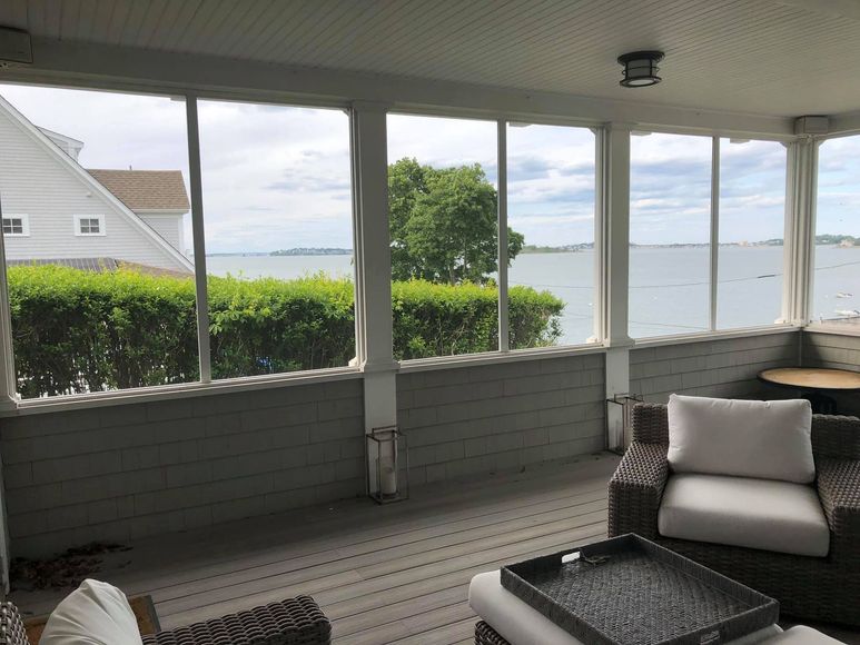 Screened porch with water view, wicker furniture, and house in the background.