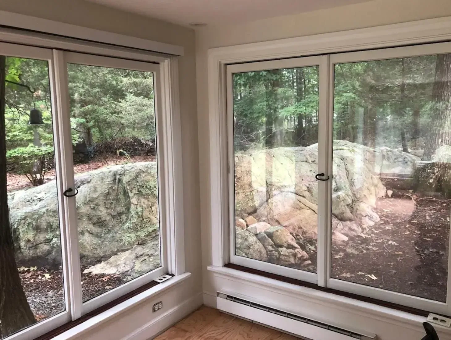 Two windows with white frames overlooking a wooded area and large rock.