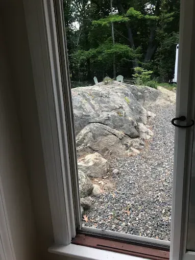 View through a doorway of a large gray rock and gravel path, surrounded by greenery.