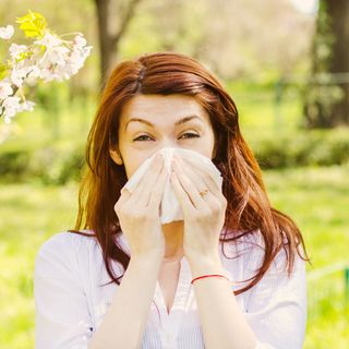 Woman sneezing into tissue paper outdoors