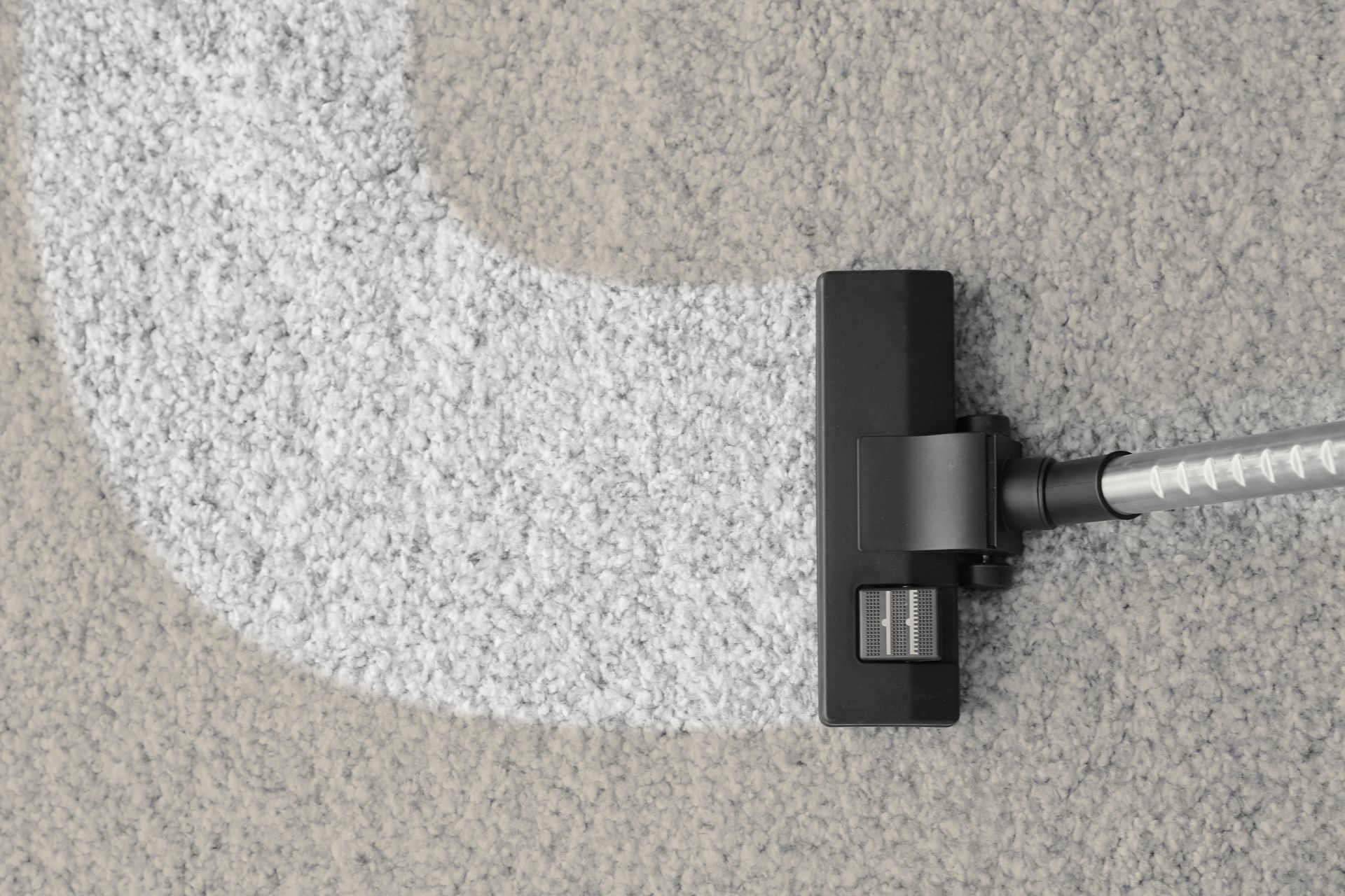 Vacuum cleaner cleaning a light gray carpet, leaving a clean white path.