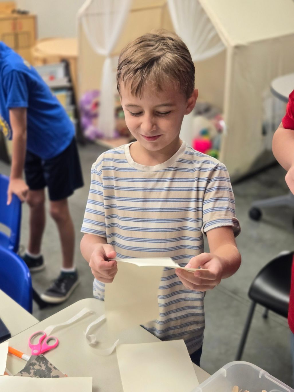 A young boy is sitting at a table holding a piece of paper.
