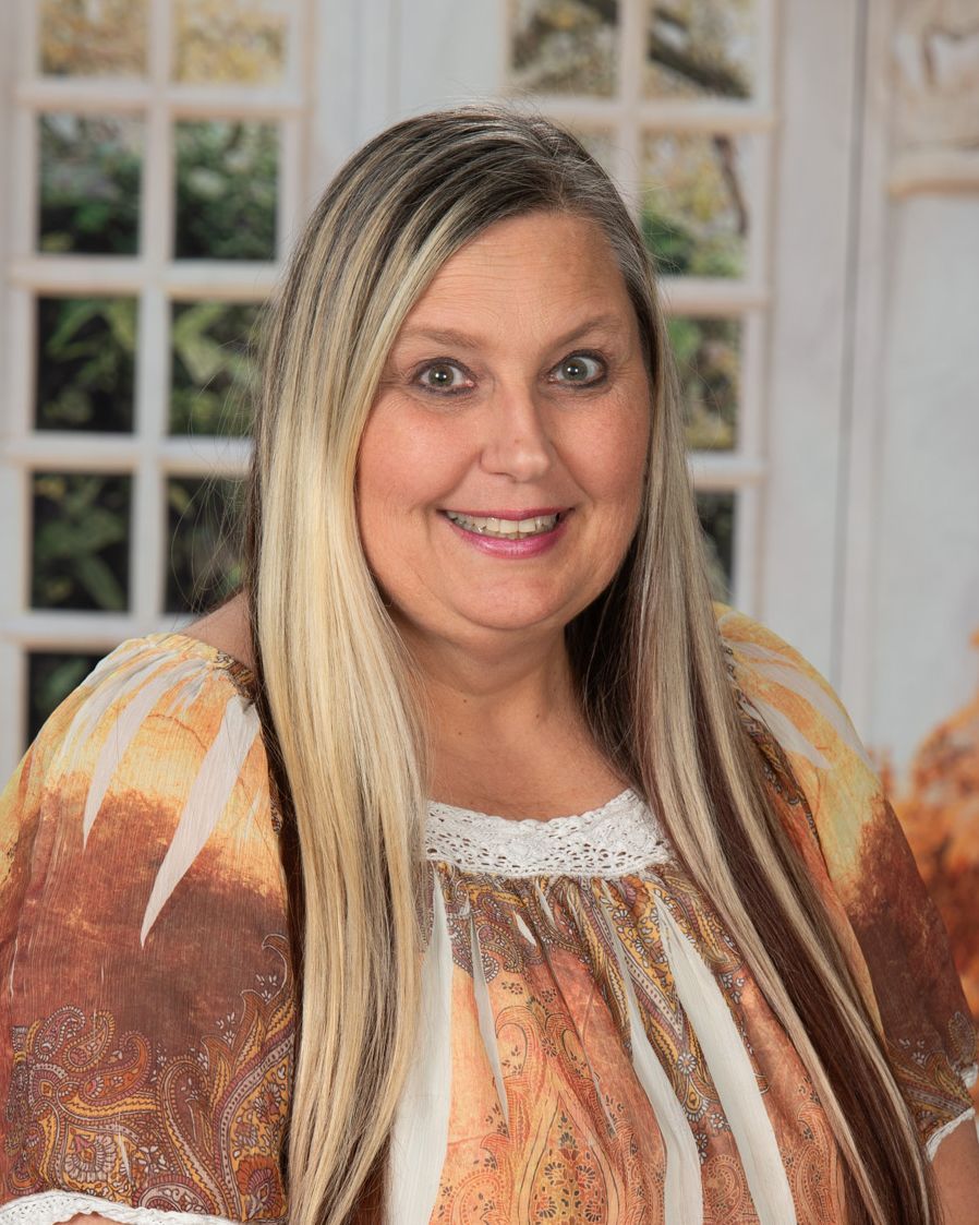 A woman with long blonde hair is wearing a pink shirt and smiling.