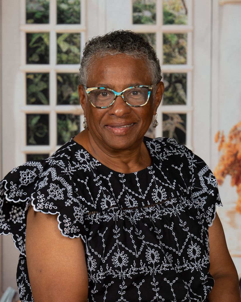A woman wearing glasses and a red floral shirt is smiling for the camera.