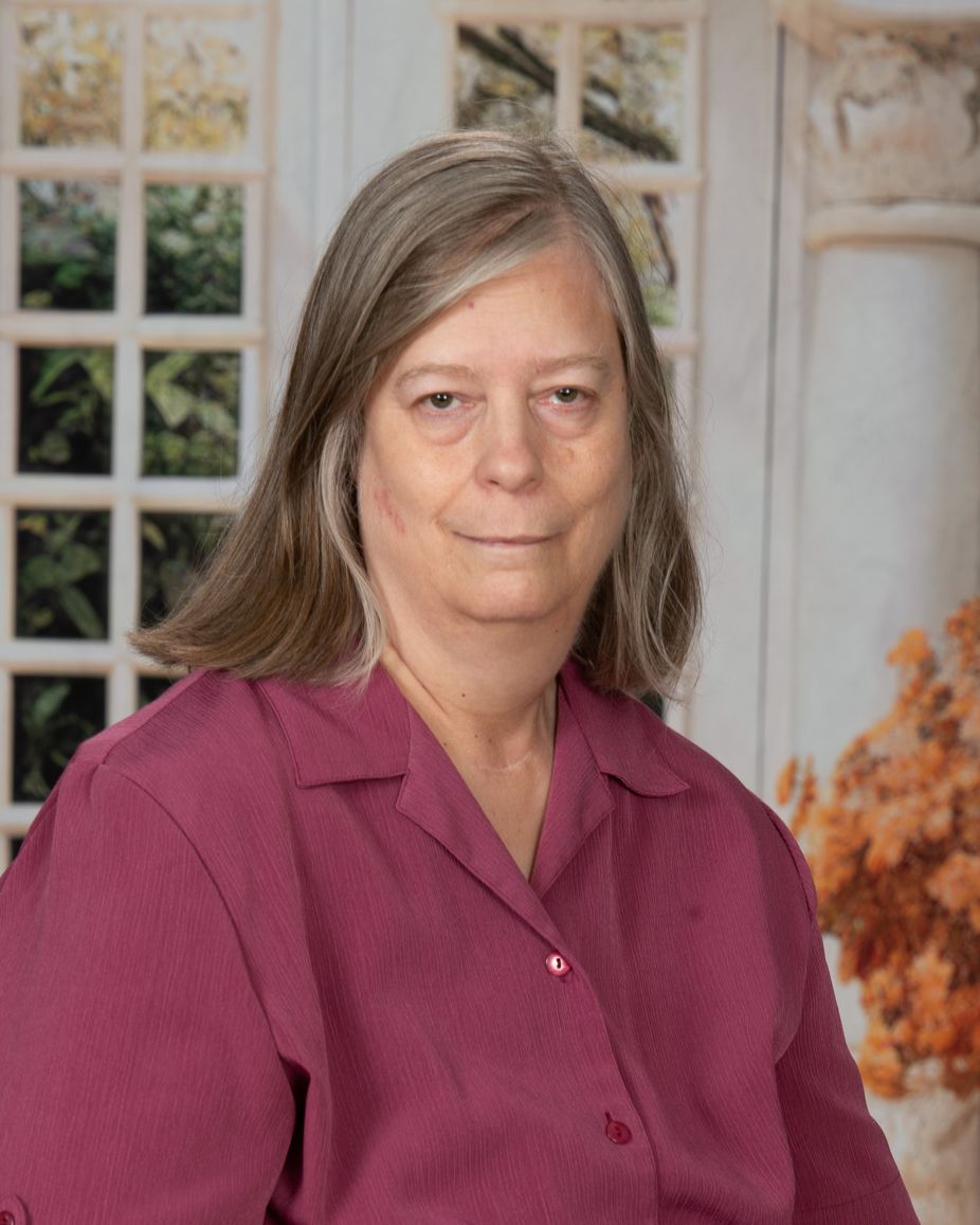 A woman in a pink shirt is looking at the camera.