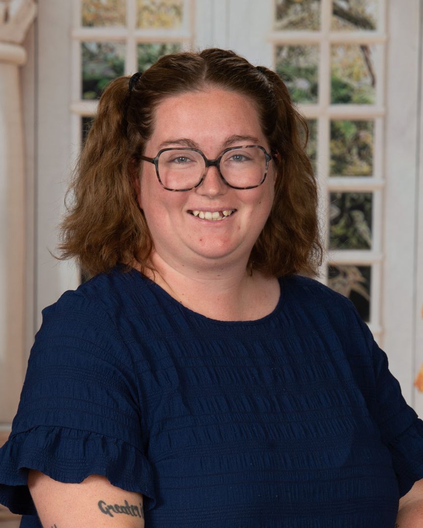 A woman wearing glasses and a blue shirt is smiling for the camera.