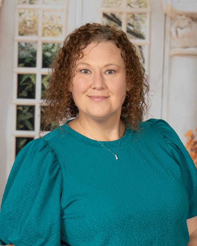 A woman with curly hair is smiling and wearing a blue shirt