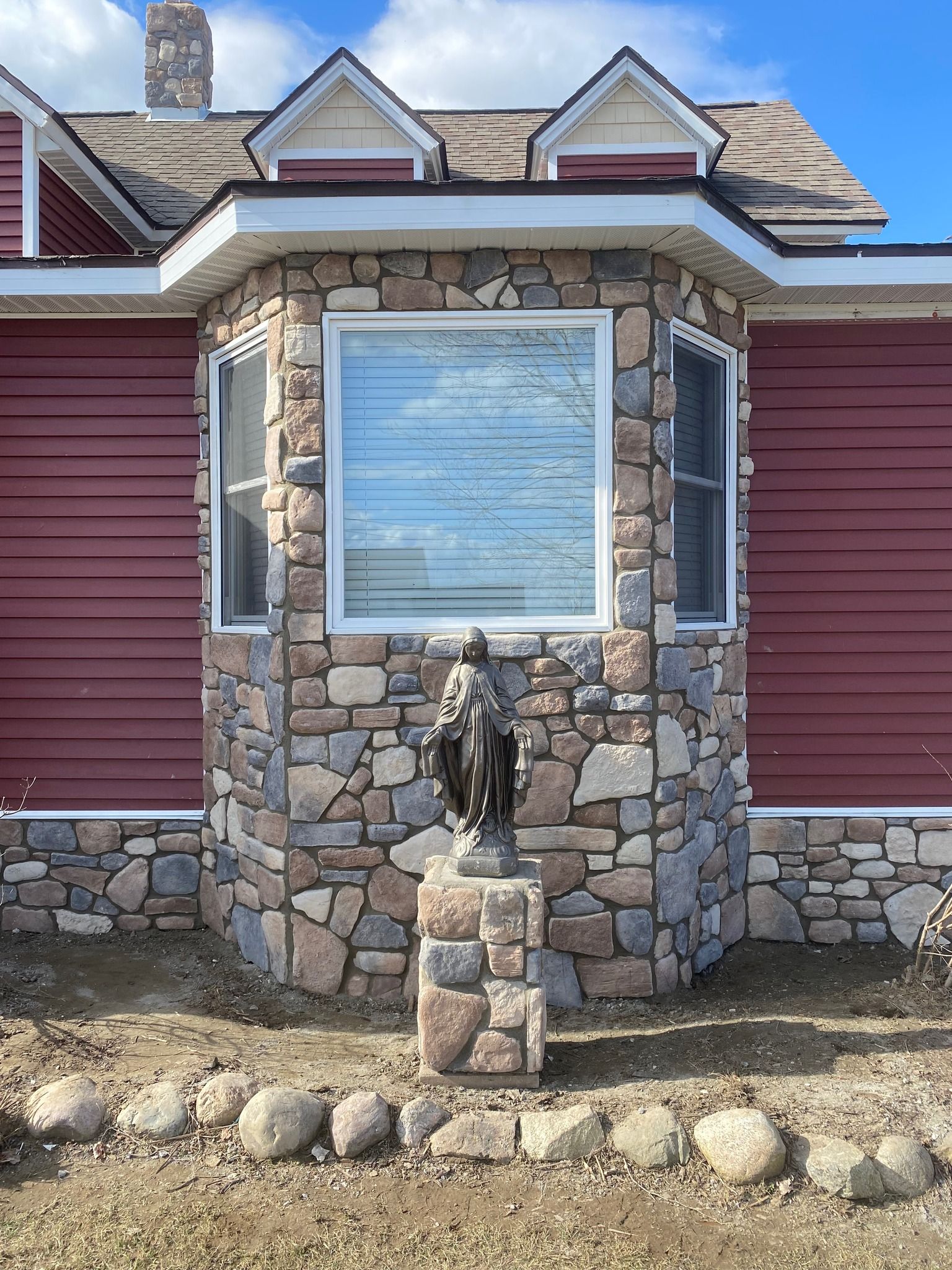 A red house with a stone wall and a statue in front of it.