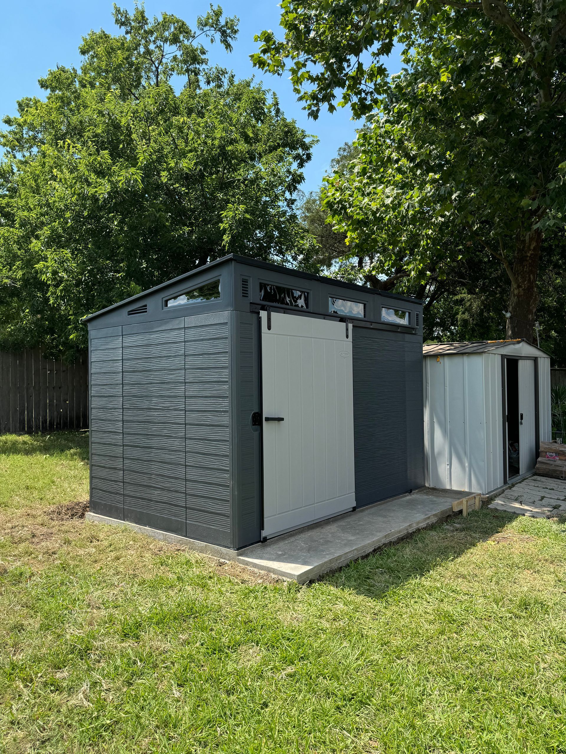 A gray and white shed is sitting in the middle of a grassy yard.