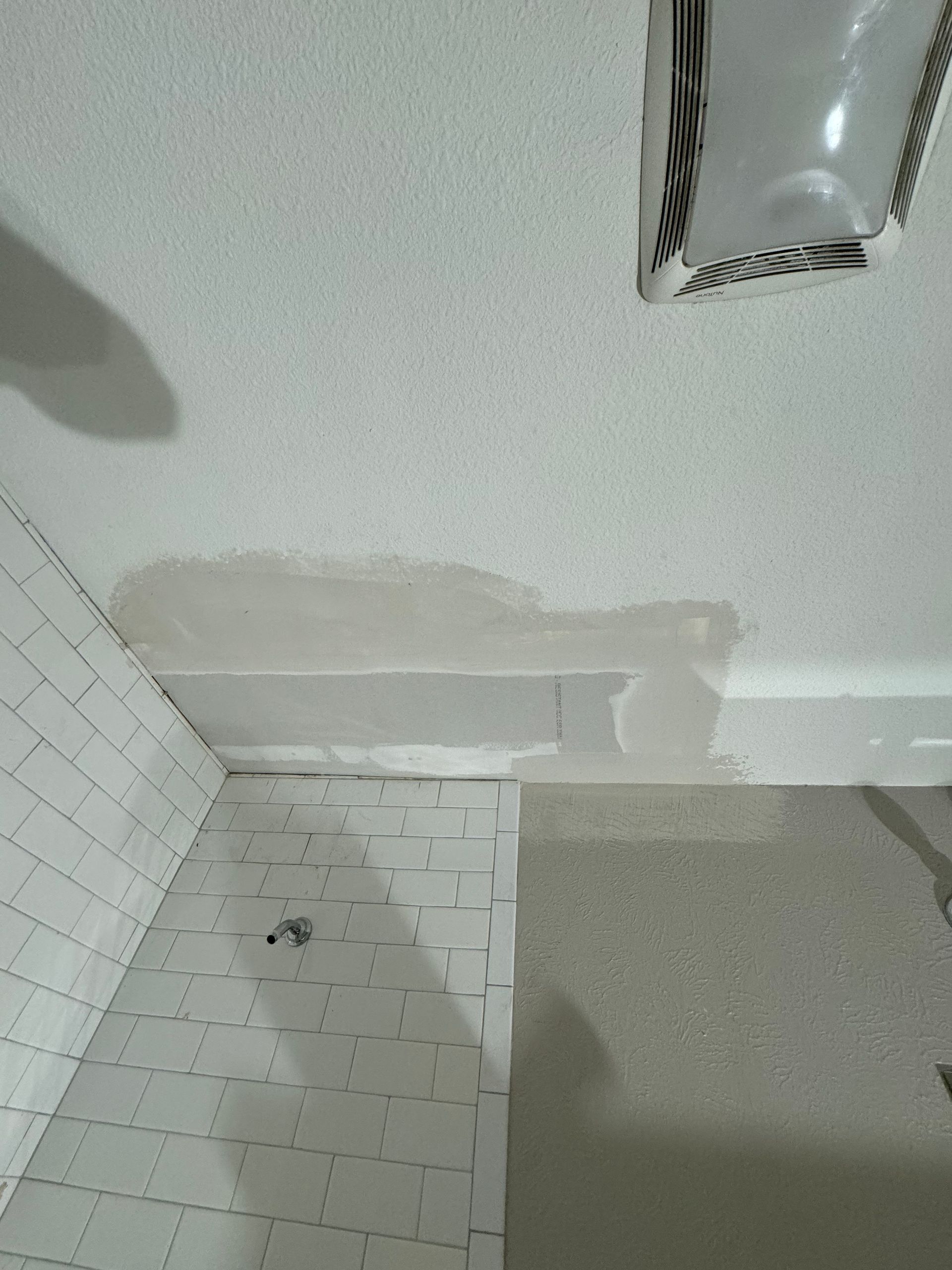 A bathroom with white tiles and a fan on the ceiling