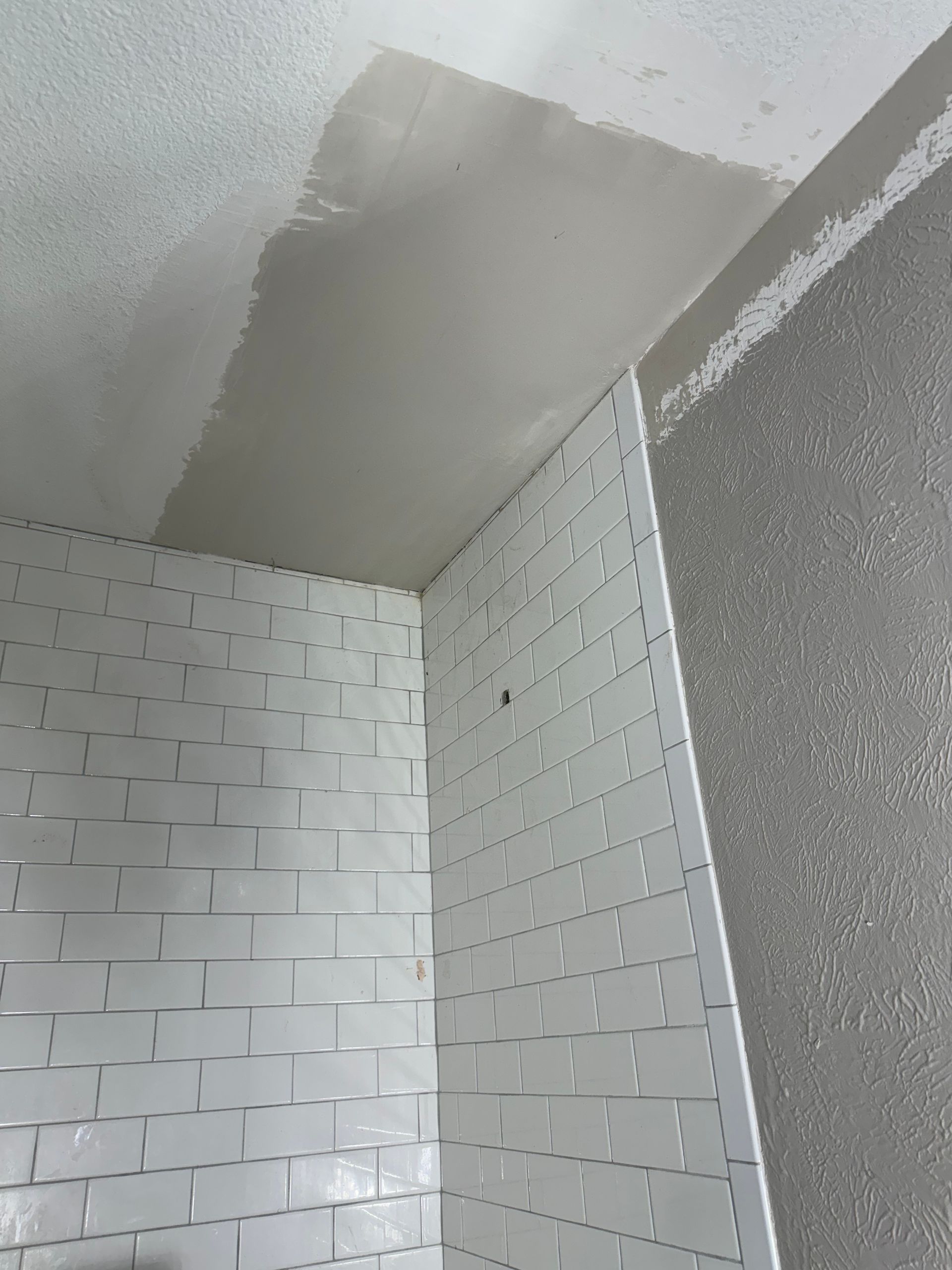A corner of a room with white tiles and a ceiling