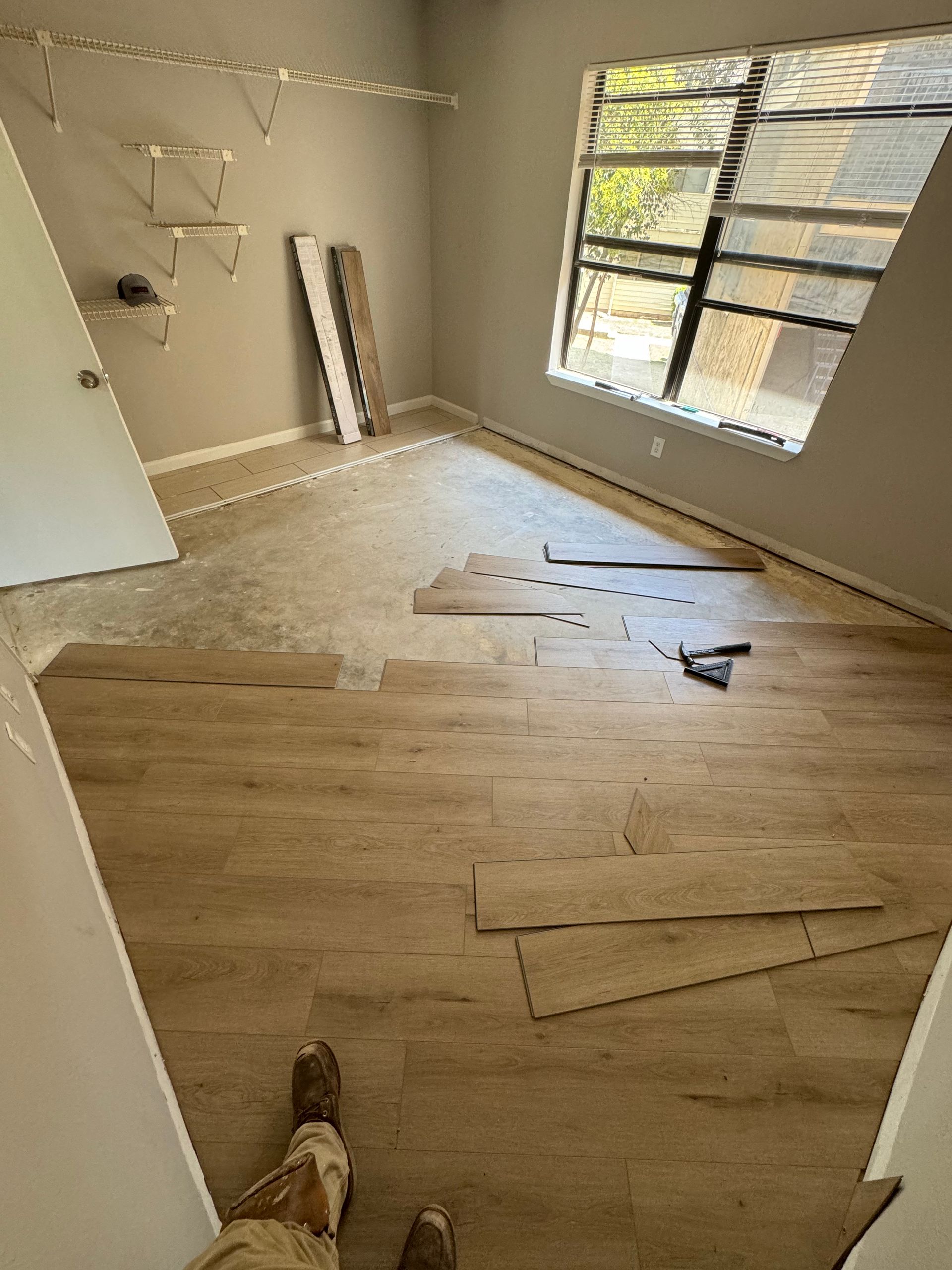 A person is standing on a wooden floor in a room with a window.