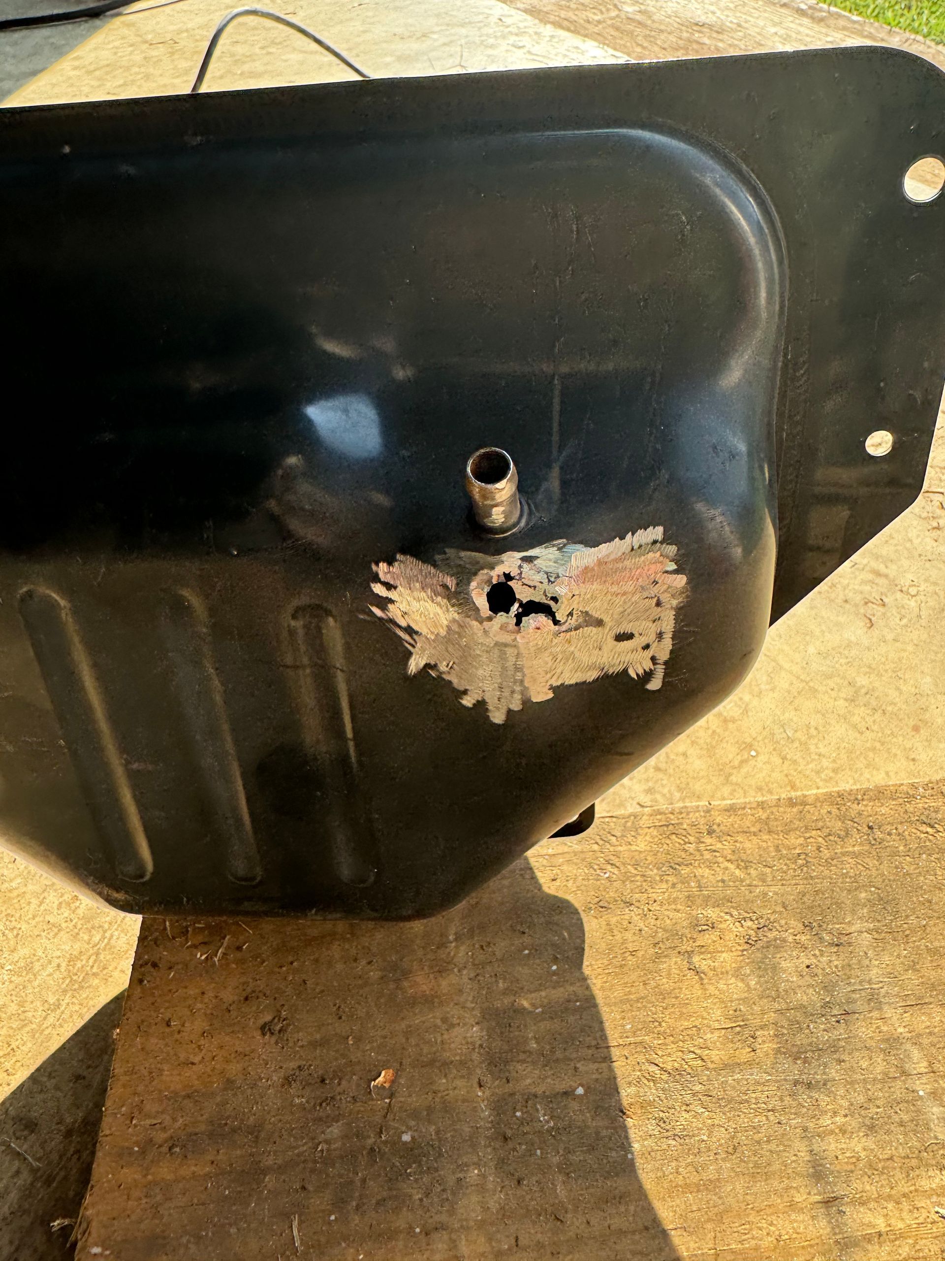 A black fuel tank with a hole in it is sitting on the ground.