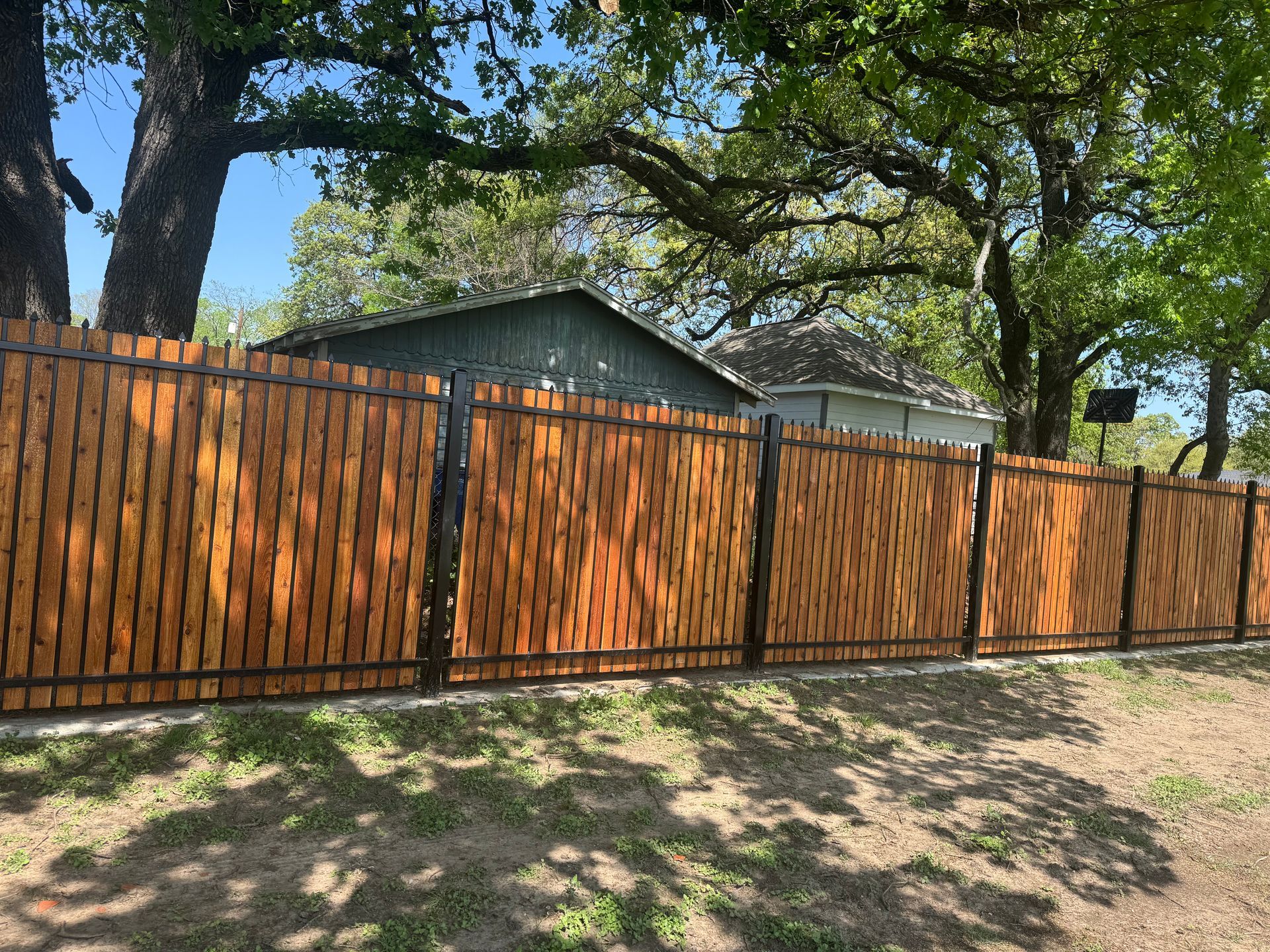 A wooden fence is surrounded by trees and grass in front of a house.
