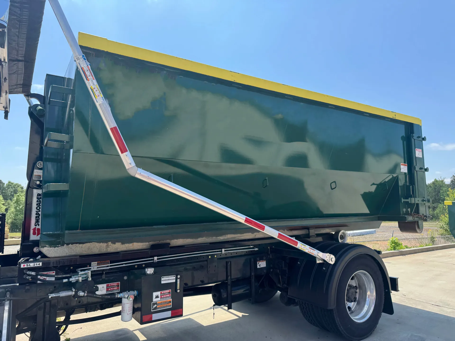 A green dump truck with a yellow top is parked on the side of the road.