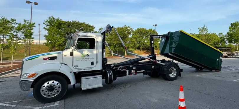 A dump truck with a green dumpster attached to it is parked in a parking lot.