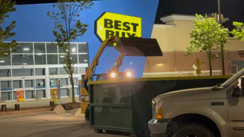 A dumpster is parked in front of a best buy store.