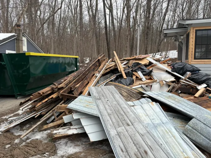 A pile of wood and metal is sitting in front of a dumpster.