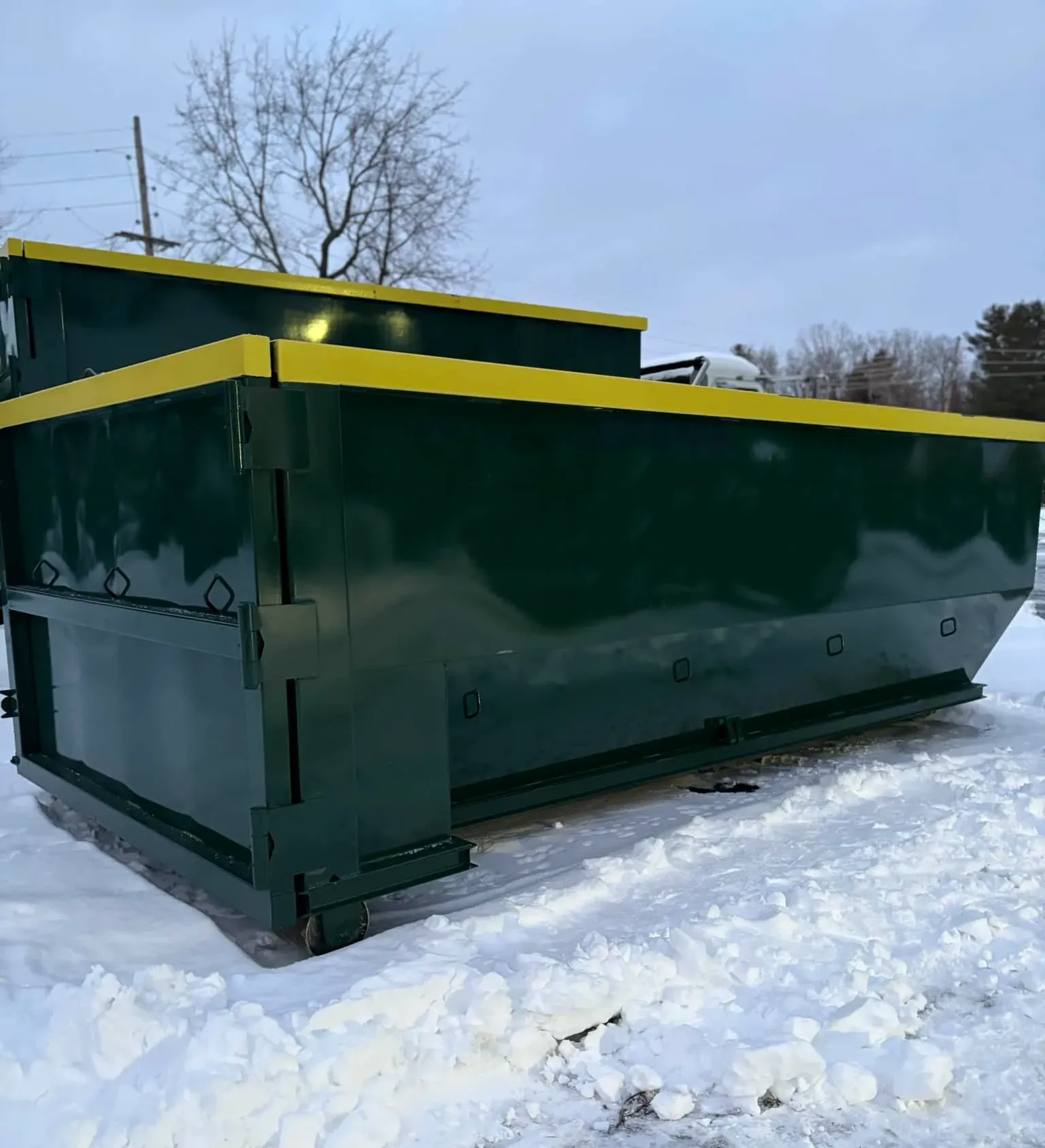 A green dumpster with a yellow trim sits in the snow