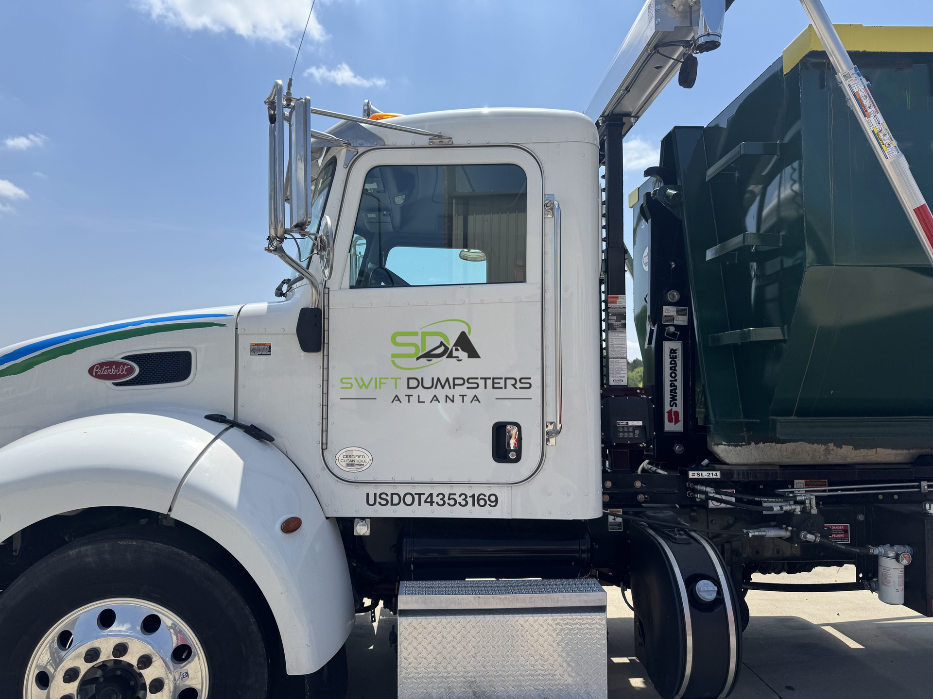 A white garbage truck with a green dumpster attached to it is parked on the side of the road.