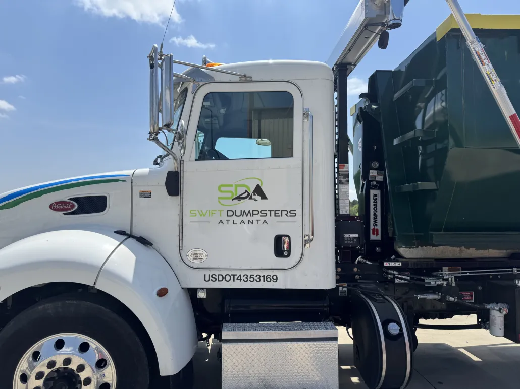 A white garbage truck with a green dumpster attached to it is parked in a parking lot.