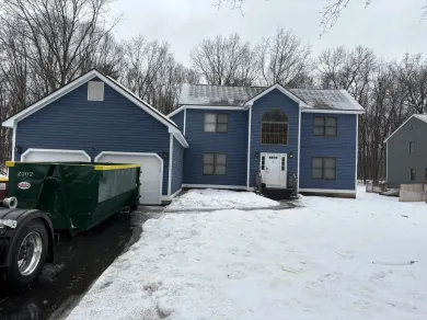 A dumpster is parked in front of a blue house covered in snow.