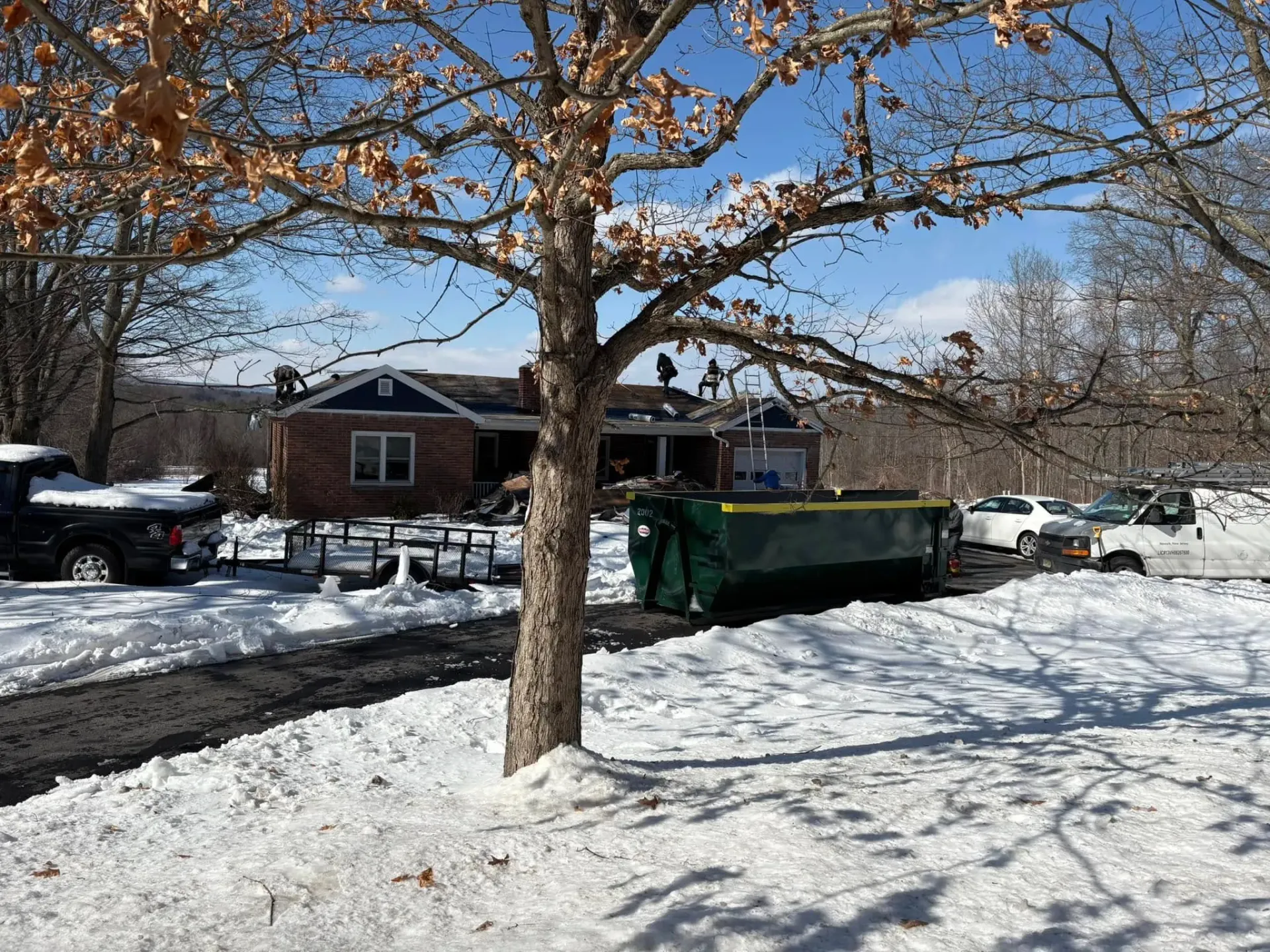 A dumpster is parked in the snow in front of a house.