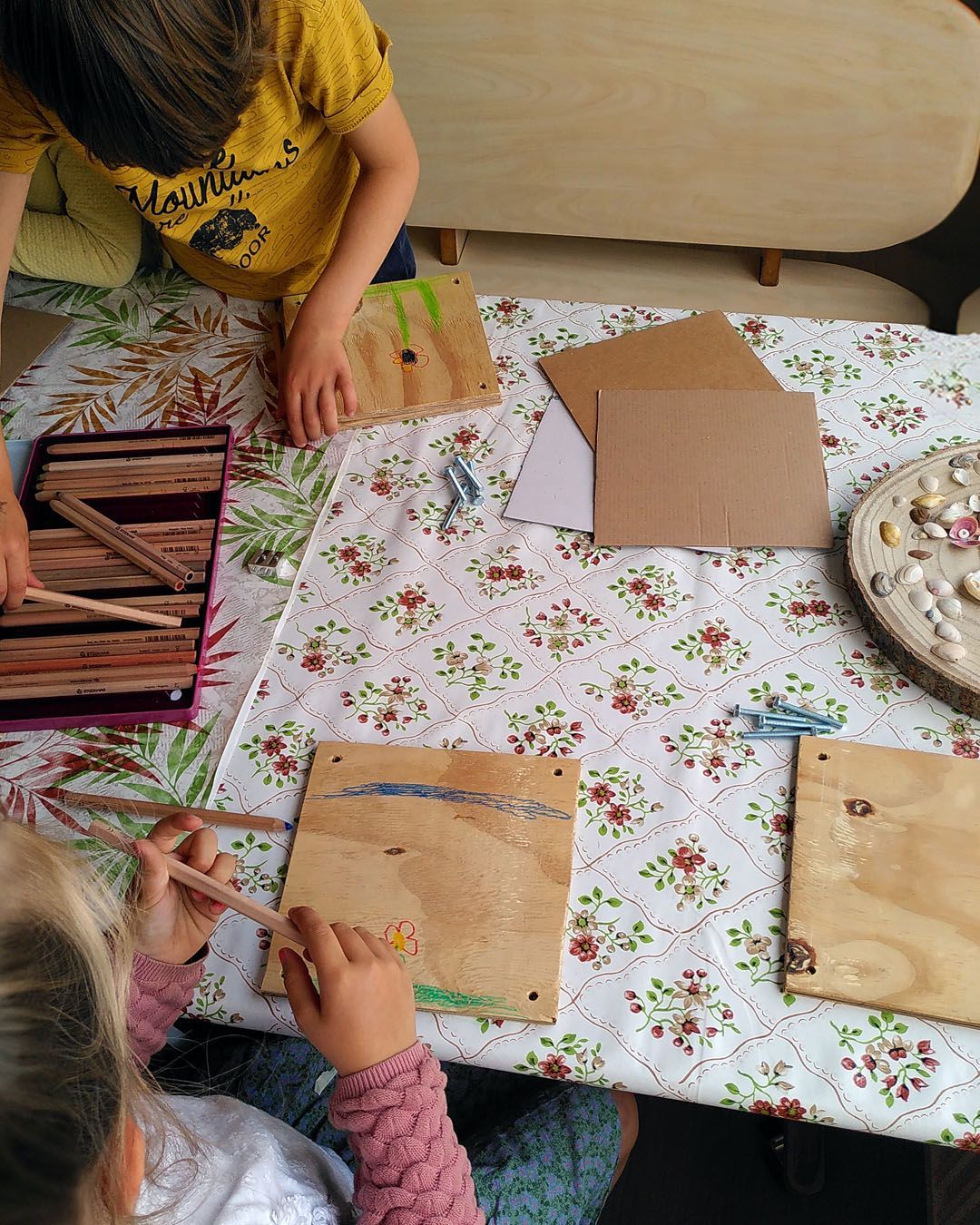 Een jongen en een meisje zitten aan een tafel een bloemenpers te maken. Atelierkinderen, atelier Verda.