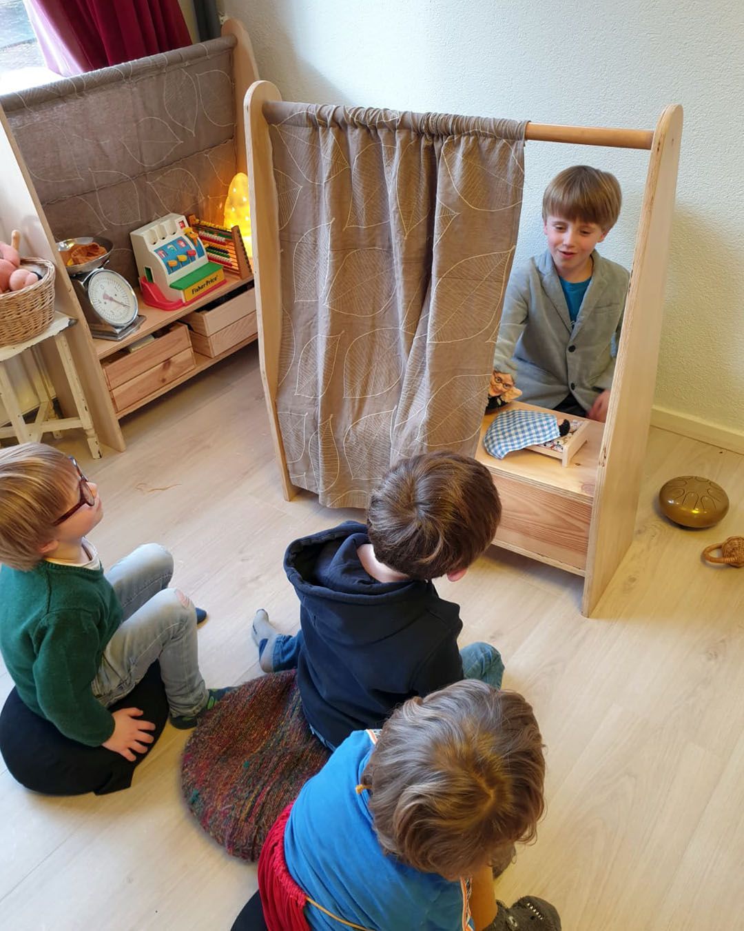 Een groepje kinderen zit op de grond voor het theater. De verhalen vertellers bij Atelierkinderen, atelier Verda.