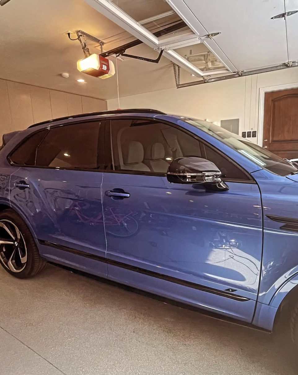 A blue car is parked in a garage with a garage door open.