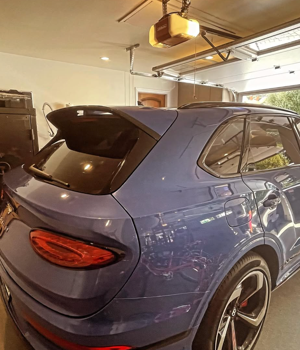 A blue bentley is parked in a garage with a garage door open.