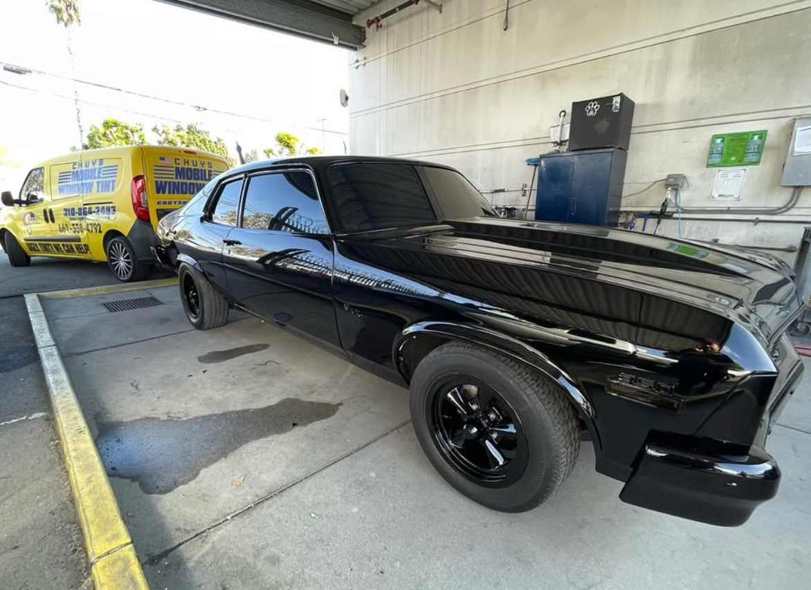 A black car is parked in a garage next to a yellow van.