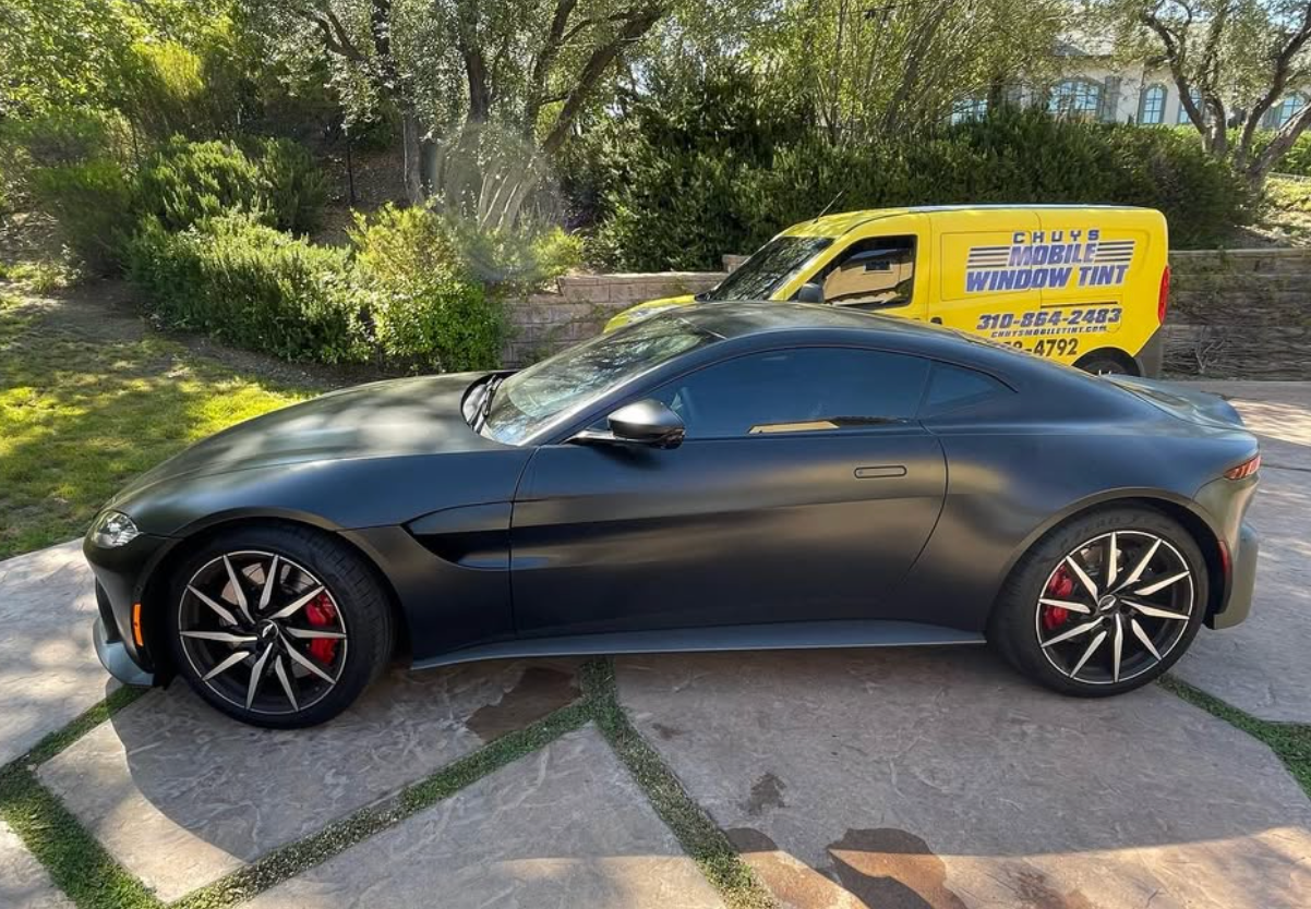 A black sports car is parked in a driveway next to a yellow van.