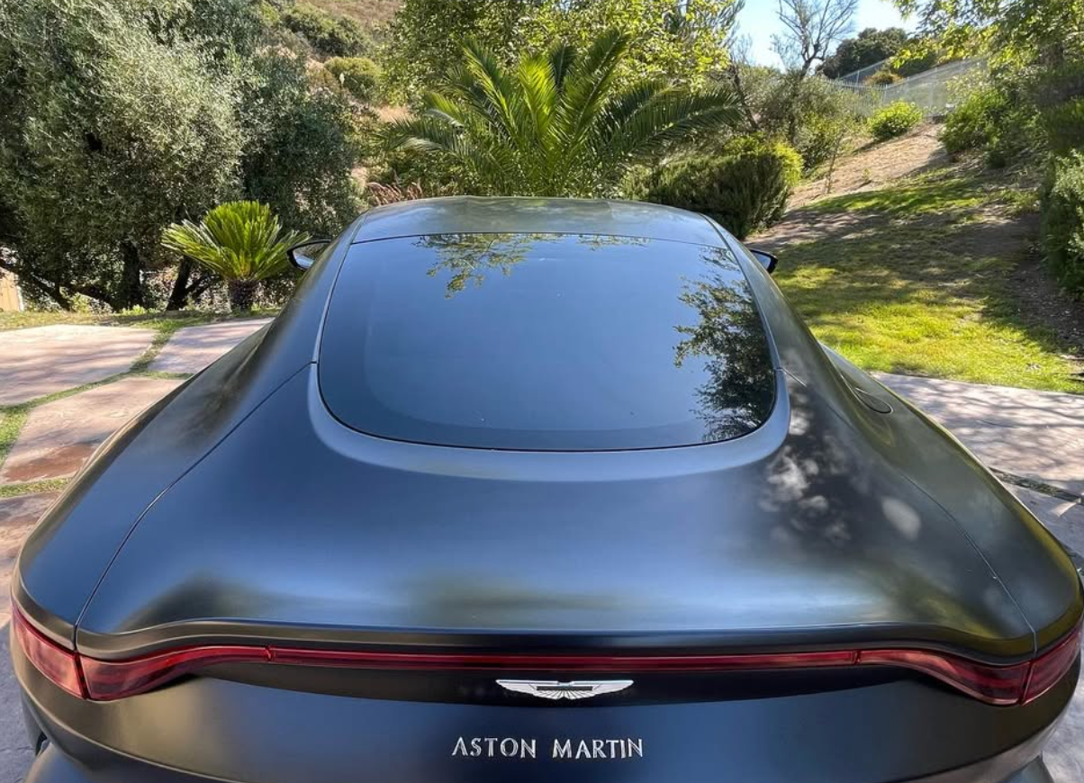 A black aston martin car is parked in a driveway.