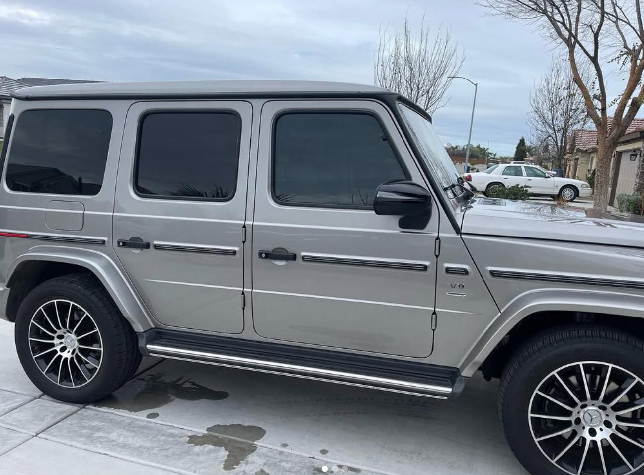 A silver mercedes benz g63 is parked on the side of the road.