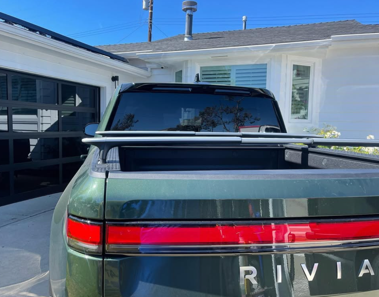 A green rivian truck is parked in front of a white house.