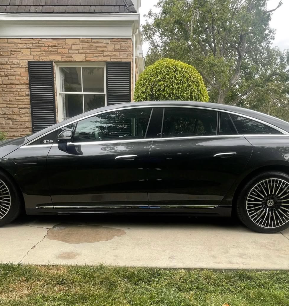 A black car is parked in front of a brick house.