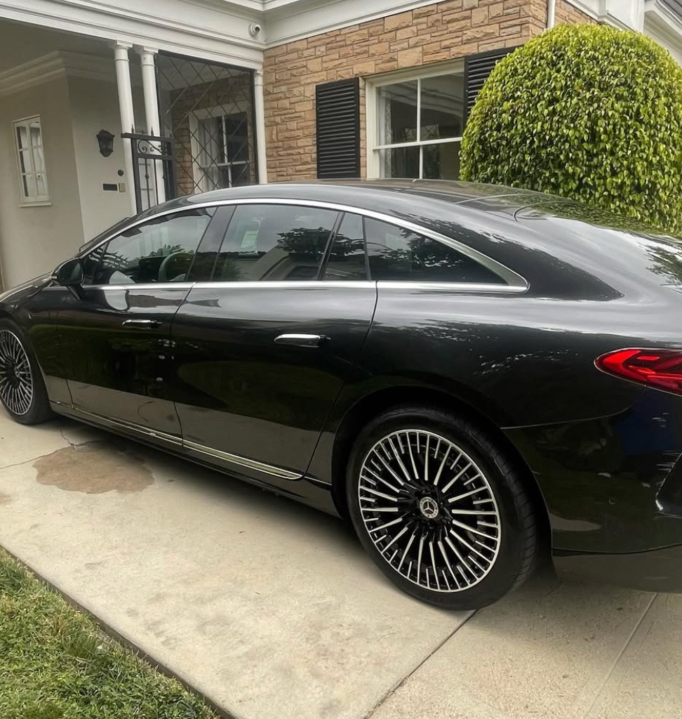 A black car is parked in front of a brick house.